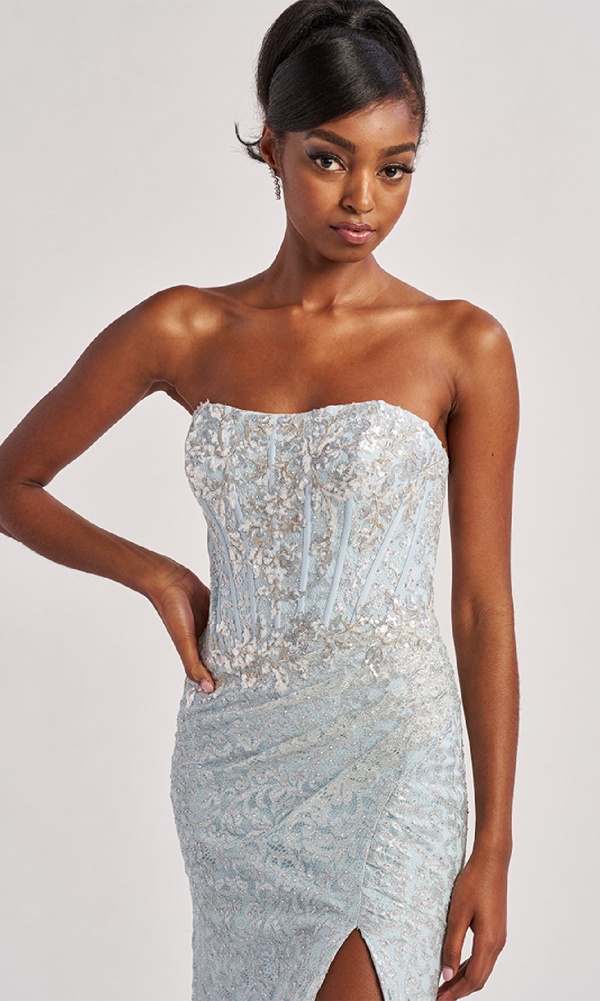 A woman poses against a plain background wearing the Long Prom Dress: Colette CL8595, a strapless light blue sequin gown with a slit.